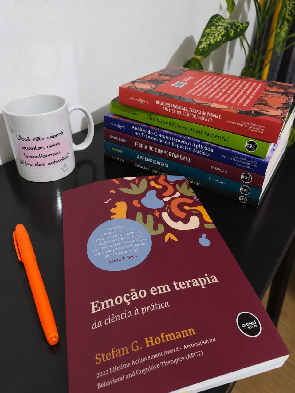 Livros de Análise do Comportamento e ACT ao lado de uma caneca com a frase: você não saberá quantas vidas transformou, mas elas saberão.